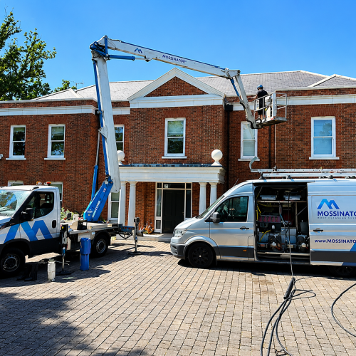 Mossinator team using a cherry picker and specialist roof cleaning equipment to clean the roof of a large residential property.