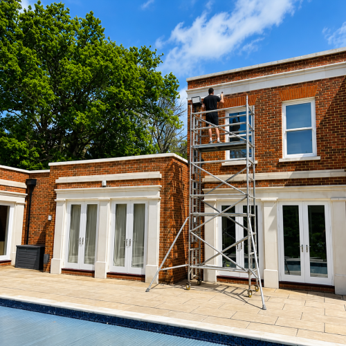 Roof cleaning technician working from a scaffold tower to safely clean and maintain the roof of a modern brick home.