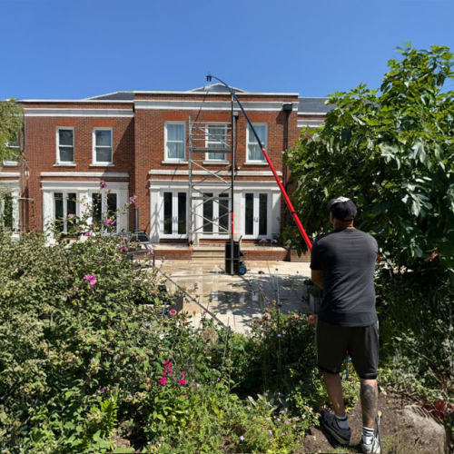 Roof cleaning technician working to clean and maintain the roof of a modern brick home.