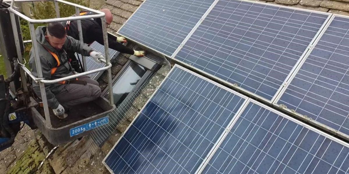 A man on a lift installs a solar panel, demonstrating renewable energy work at height.