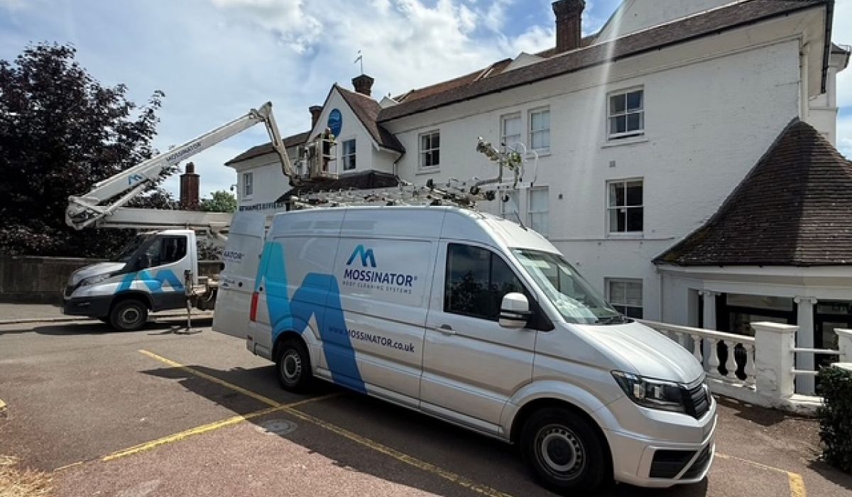 Truck-mounted cherry picker and Mossinator service van outside a hotel in Berkshire during commercial gutter clearance and high-level gutter maintenance.