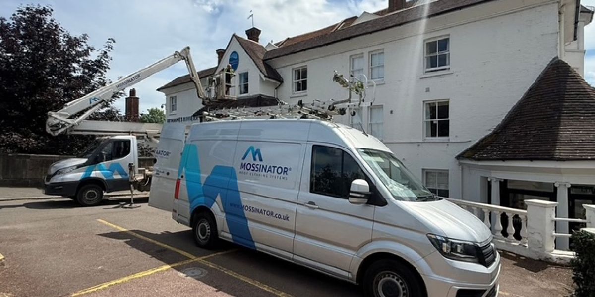 Truck-mounted cherry picker and Mossinator service van outside a hotel in Berkshire during commercial gutter clearance and high-level gutter maintenance.