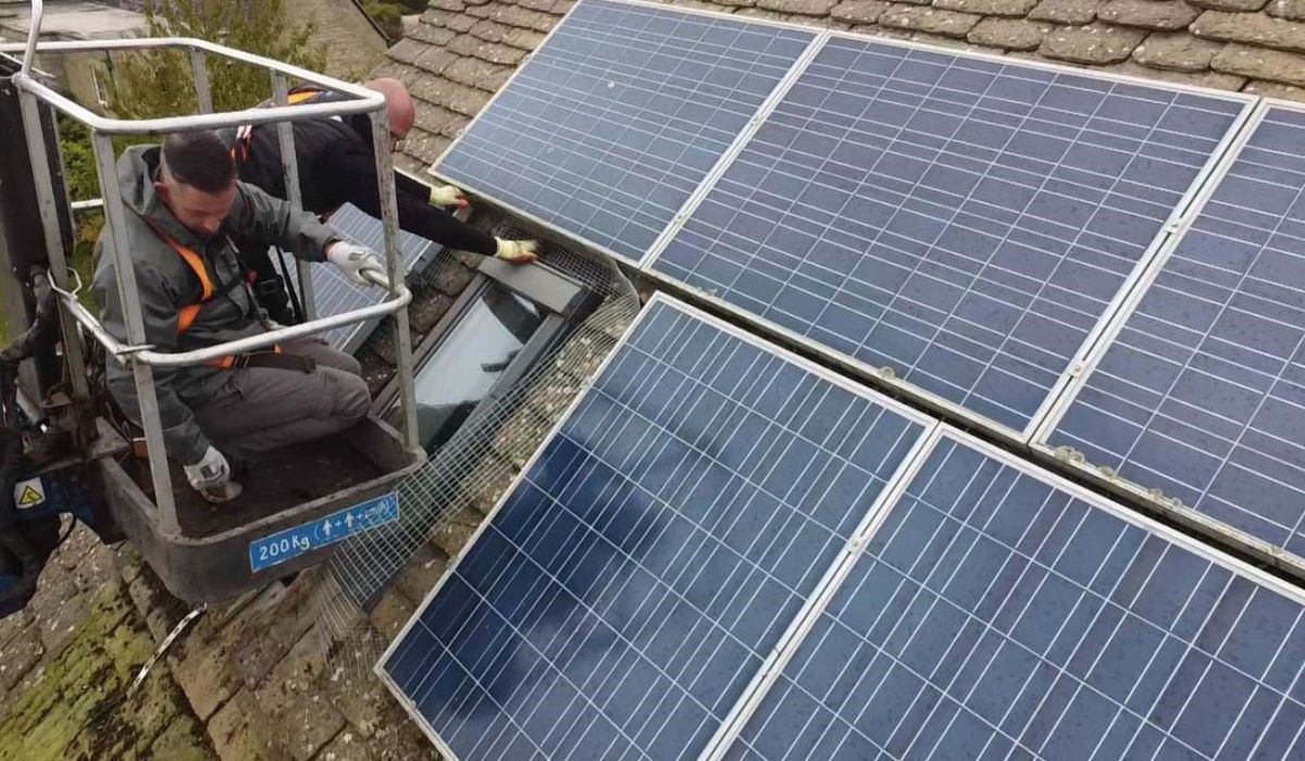 A man on a lift installs a solar panel, demonstrating renewable energy work at height.